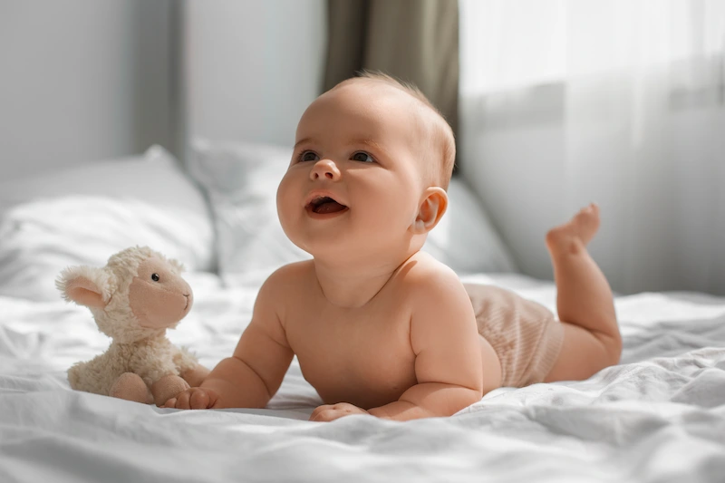 Bayi tengkurap tersenyum di atas tempat tidur