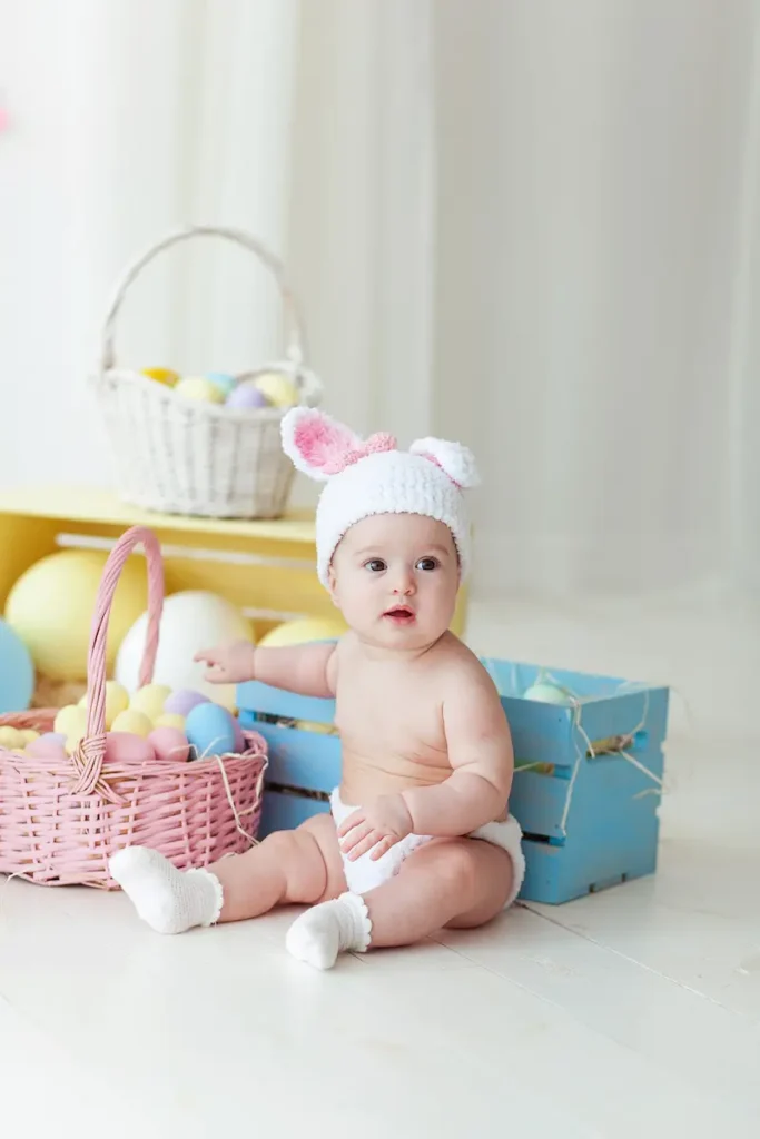 Bayi memakai topi duduk di dekat keranjang mainan