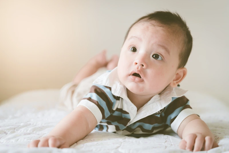 Bayi memakai baju garis hijau sedang berbaring