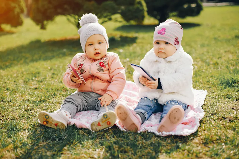 Dua bayi duduk di taman memakai topi lucu